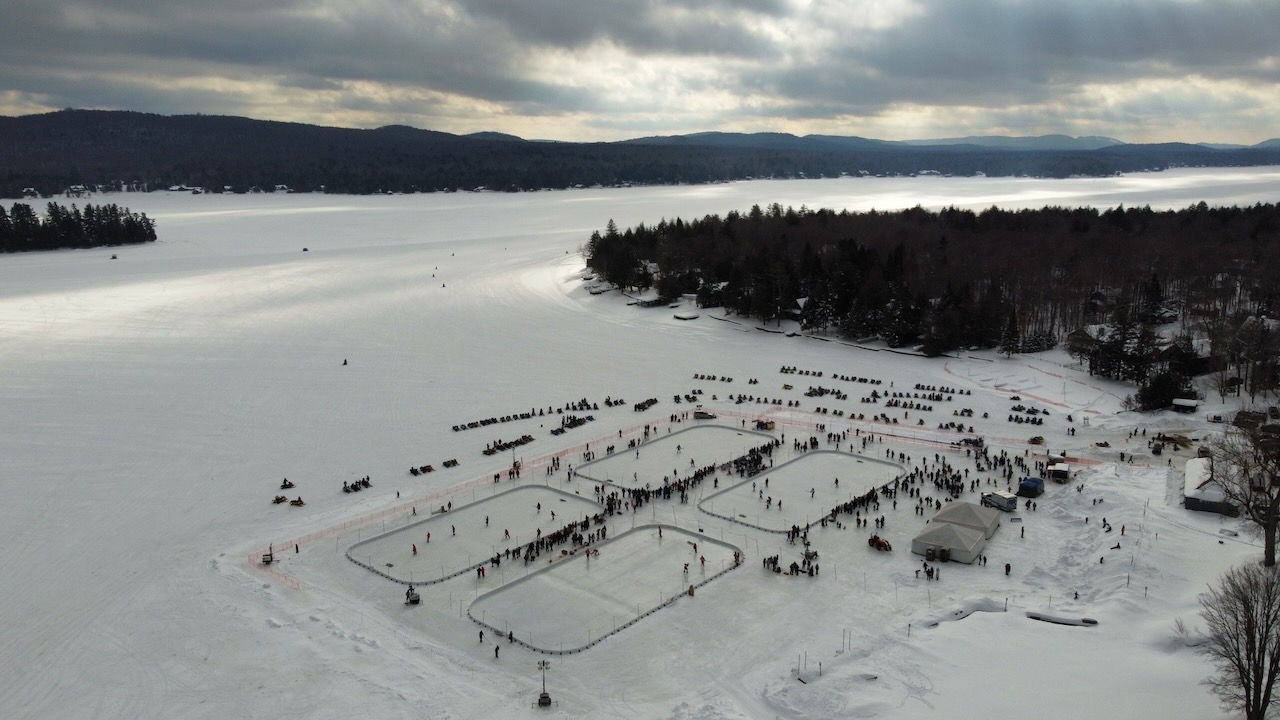 Aerial view of four ice rinks on Fourth Lake, with mountains in background. 
