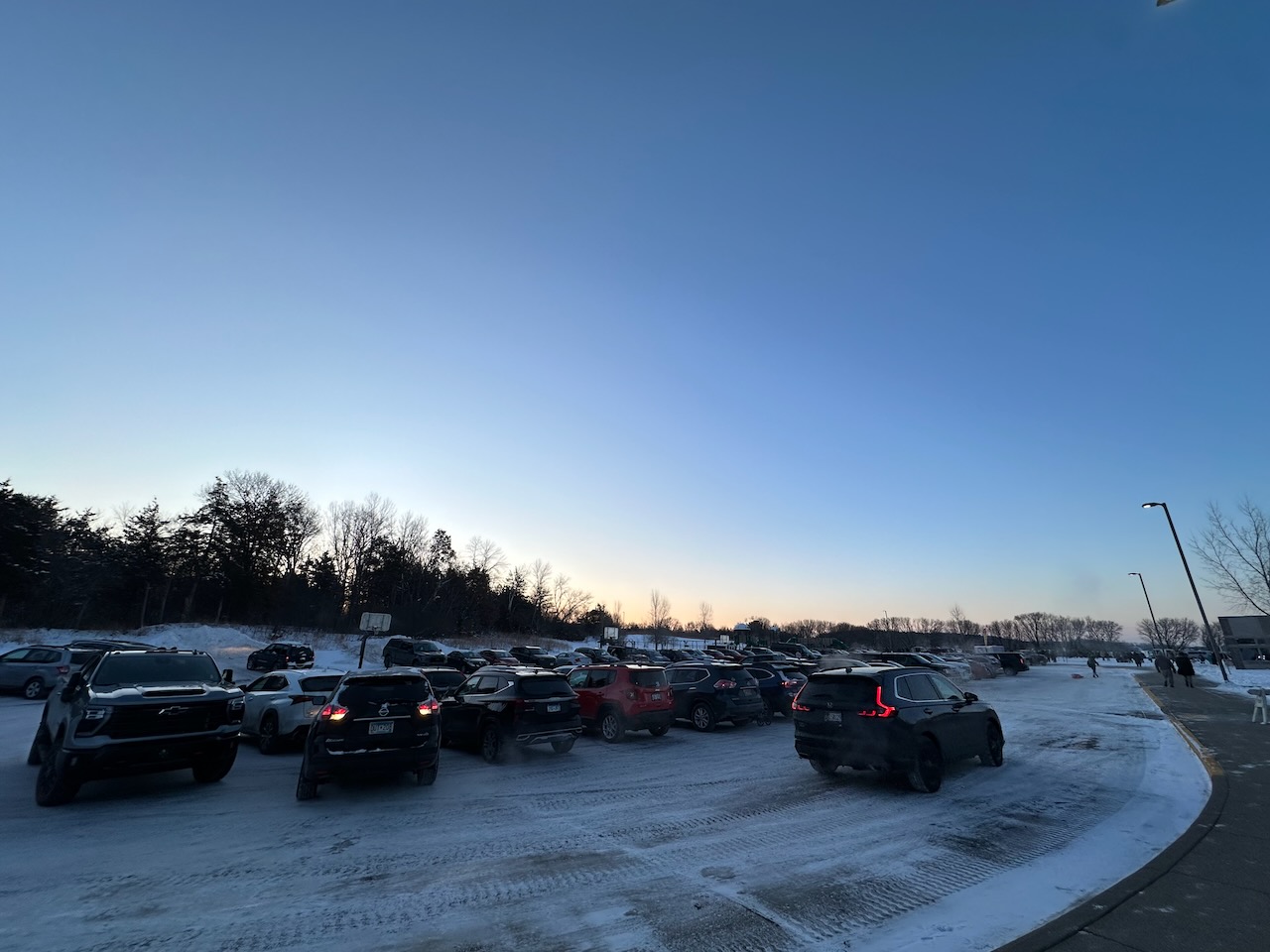 Parking lot filled with cars. The ground is covered in snow. 