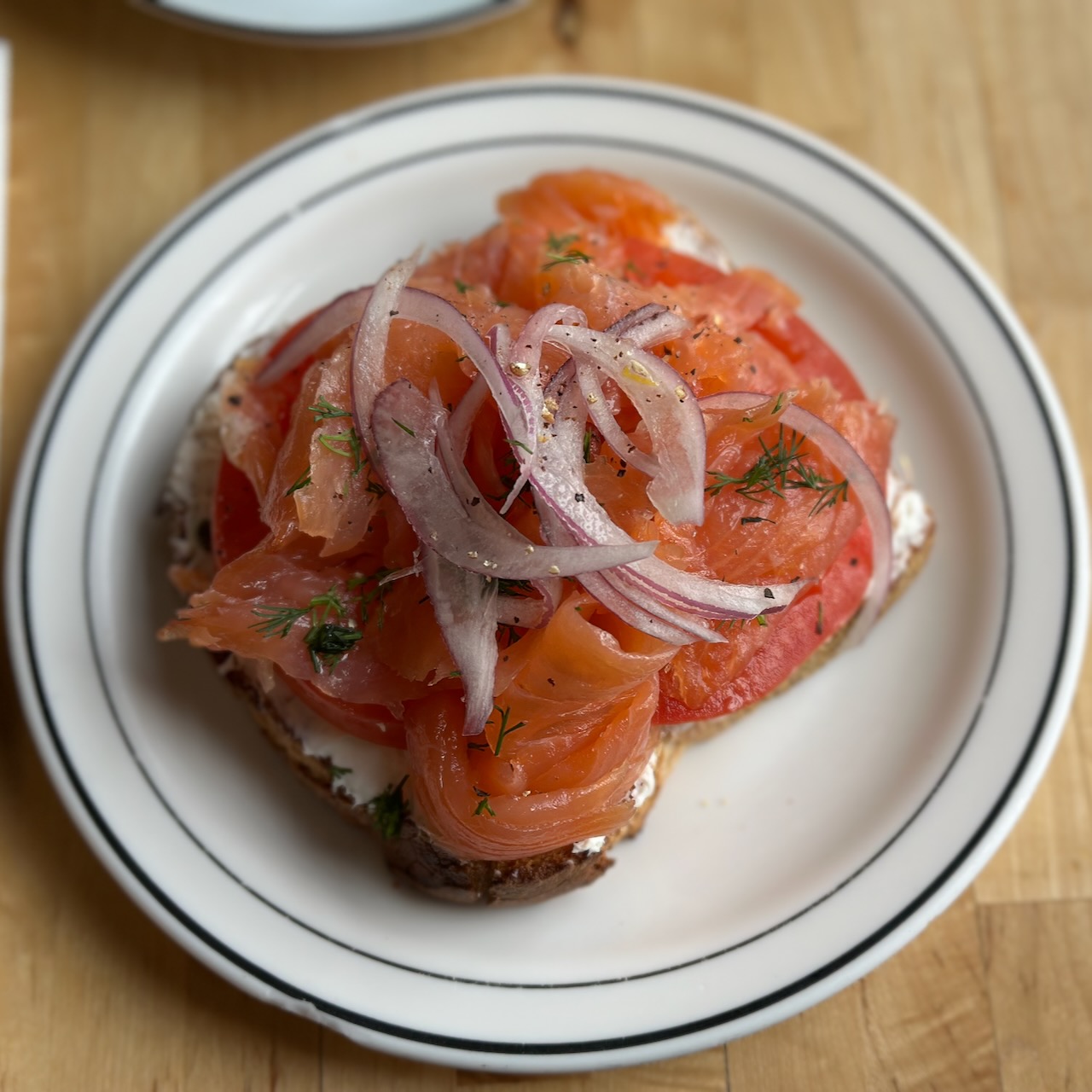 Salmon, onions, tomatoes, dill, and cream cheese on toast on a white plate. 
