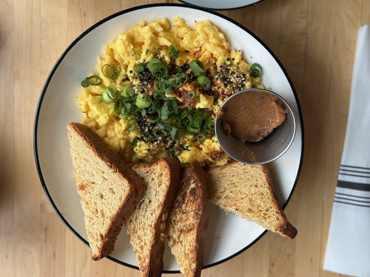 Eggs with chili sauce and gluten-free bread on white plate. The plate is on a wooden table. 