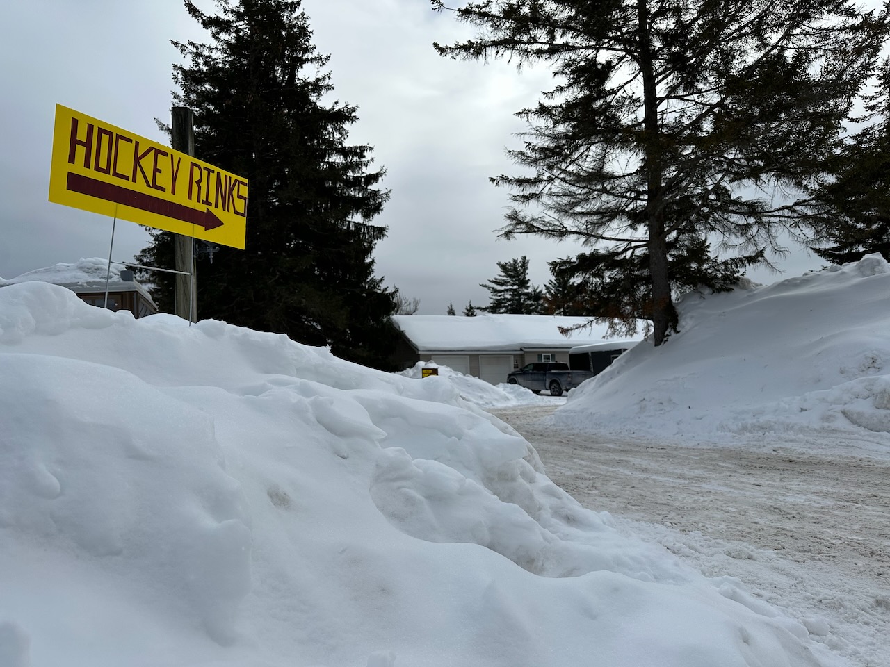 Sign on top of snow mound that says HOCKEY RINKS with an arrow pointing right.