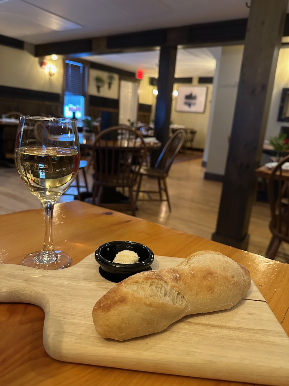 Loaf of bread on cutting board with glass of wine behind it. Both are on table. 