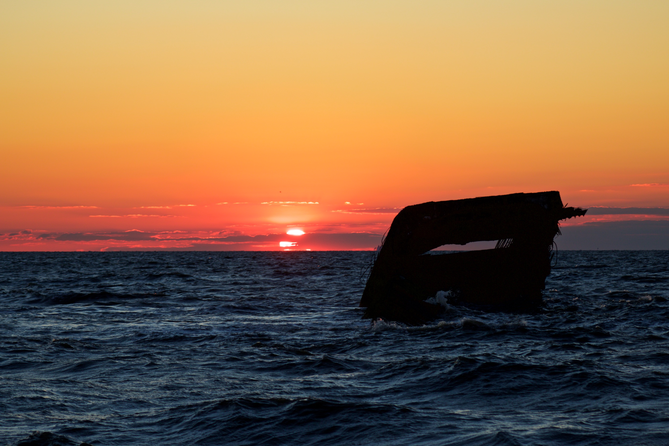 Sunset over ocean, with remains of concrete ship SS Atlantis in foreground. 