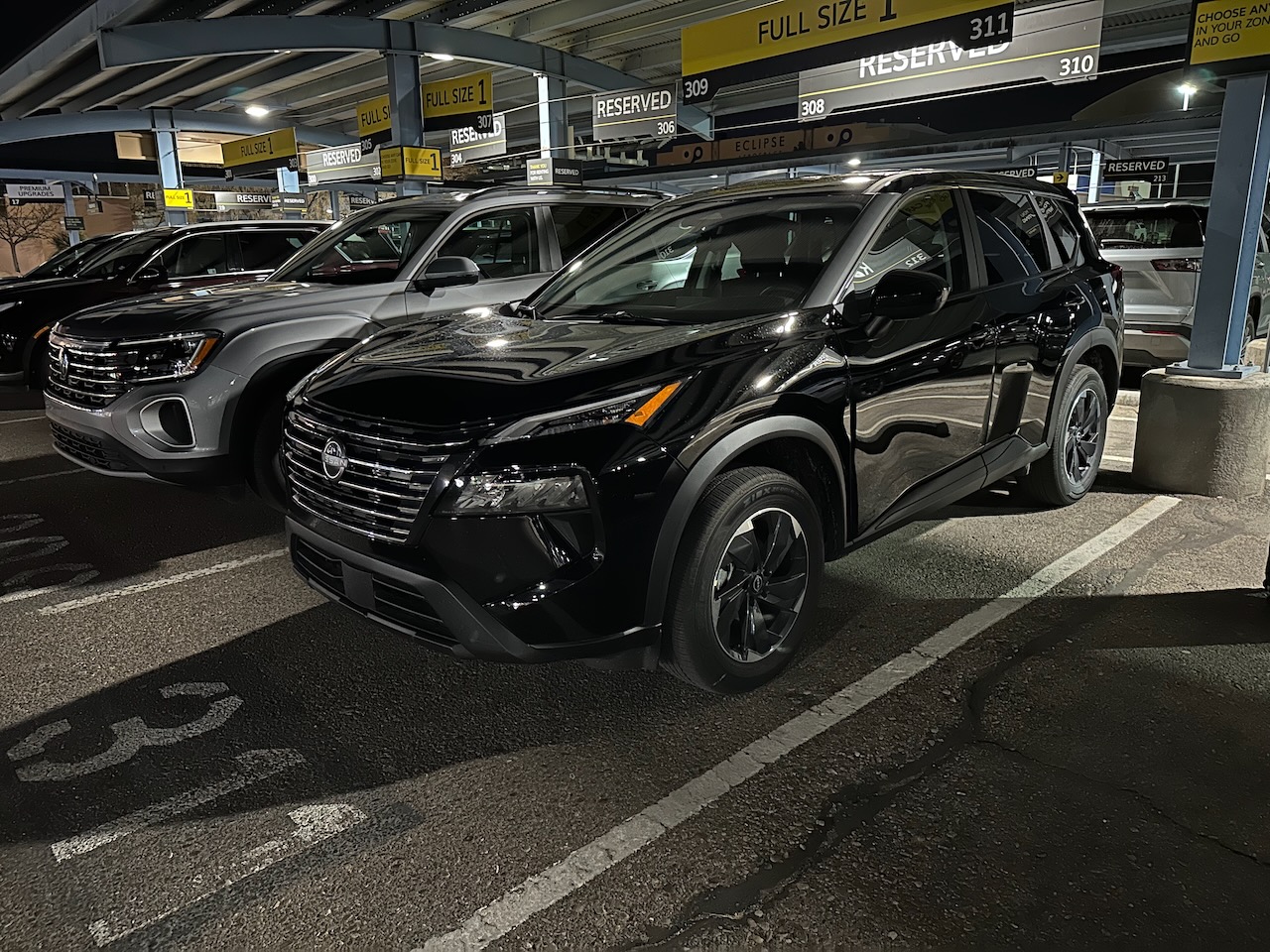 Black Nissan Rogue in rental car parking lot. 