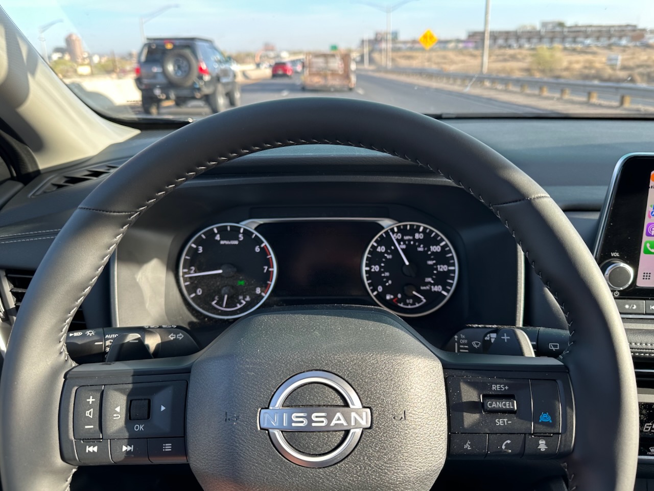 Steering wheel and gauge cluster of Nissan Rogue, with view of highway through windshield. 