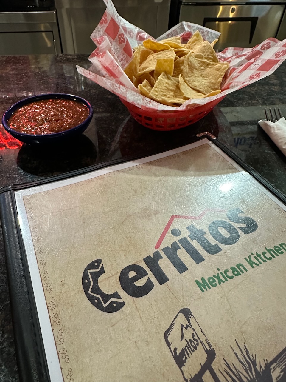 Menu with basket of chips and container of salsa on counter. 