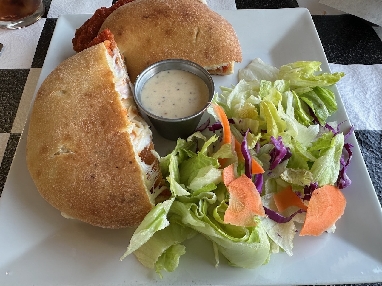Chicken parm sandwich and salad on white plate.