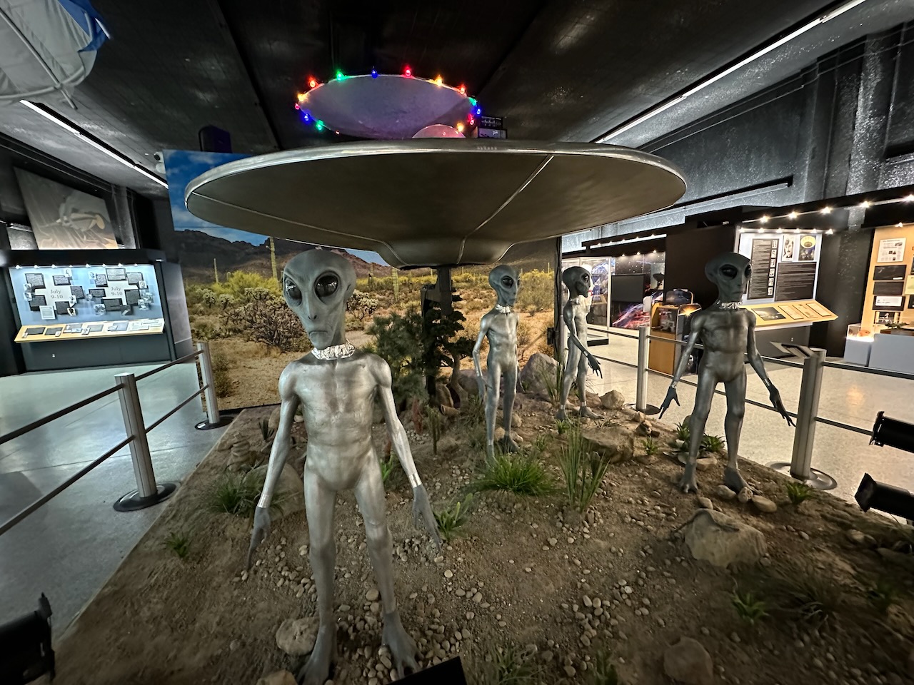 Diorama of aliens and UFO standing on green field. 