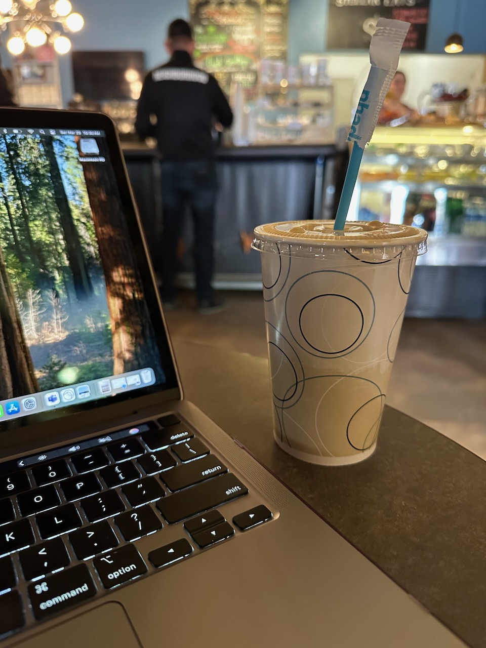 Iced oat milk latte on table next to laptop in coffee shop. 