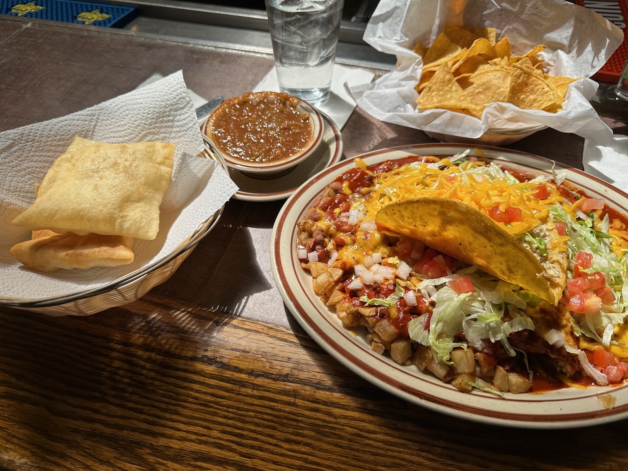 Counter with basket of chips, cup of salsa, basket of sopapillas, and platter with taco and tamale. 