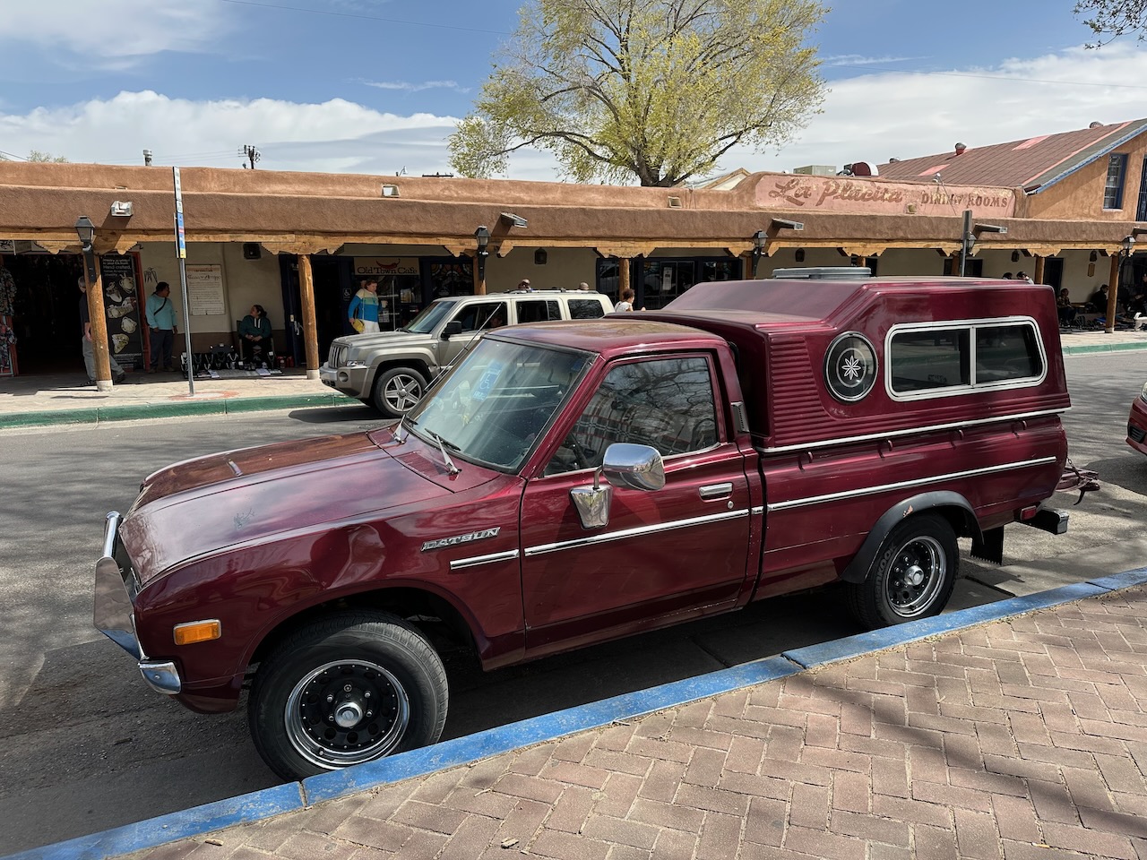 Datsun pickup truck with bed cap on side of street. 