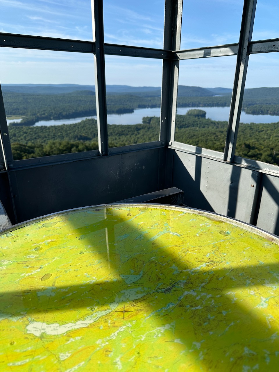 Fire table inside fire tower, with view through windows of surrounding mountains and lakes. 