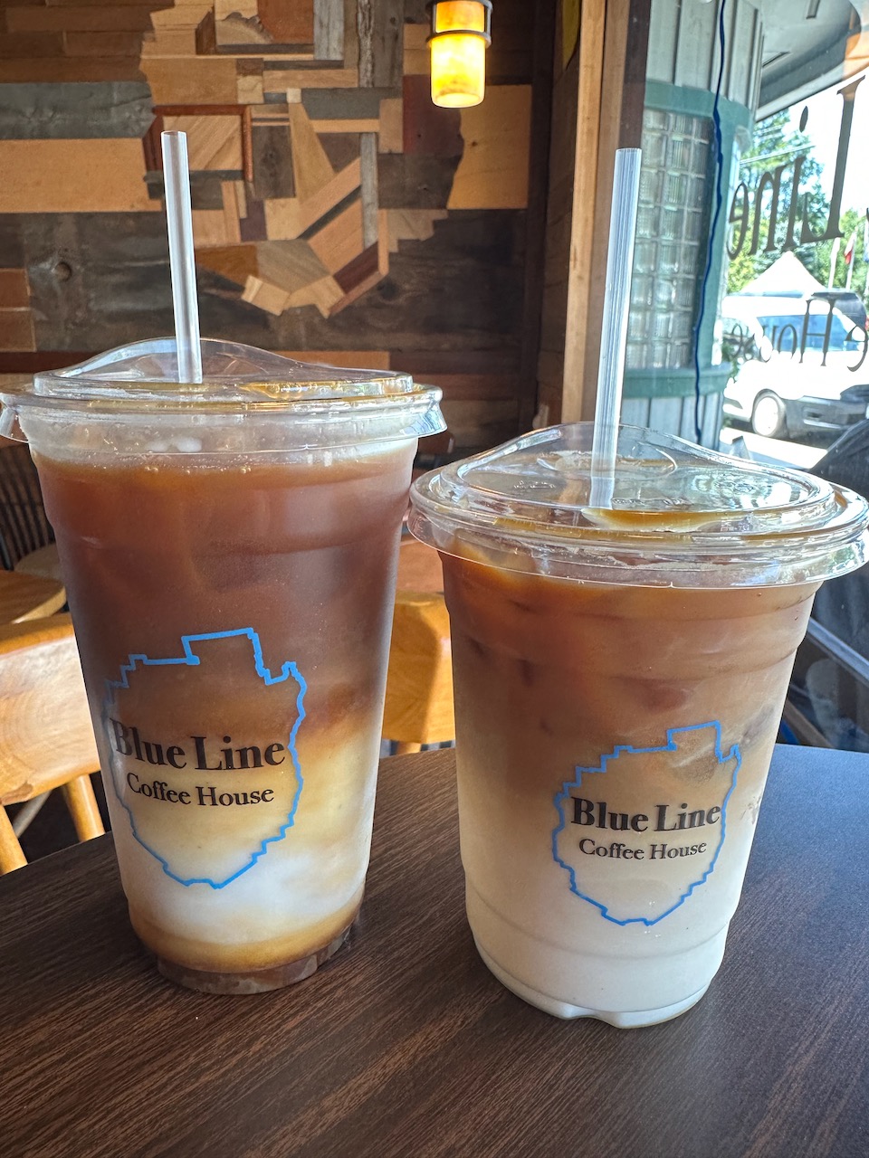Two iced coffees with plastic cups that read BLUE LINE COFFEE SHOP. 
