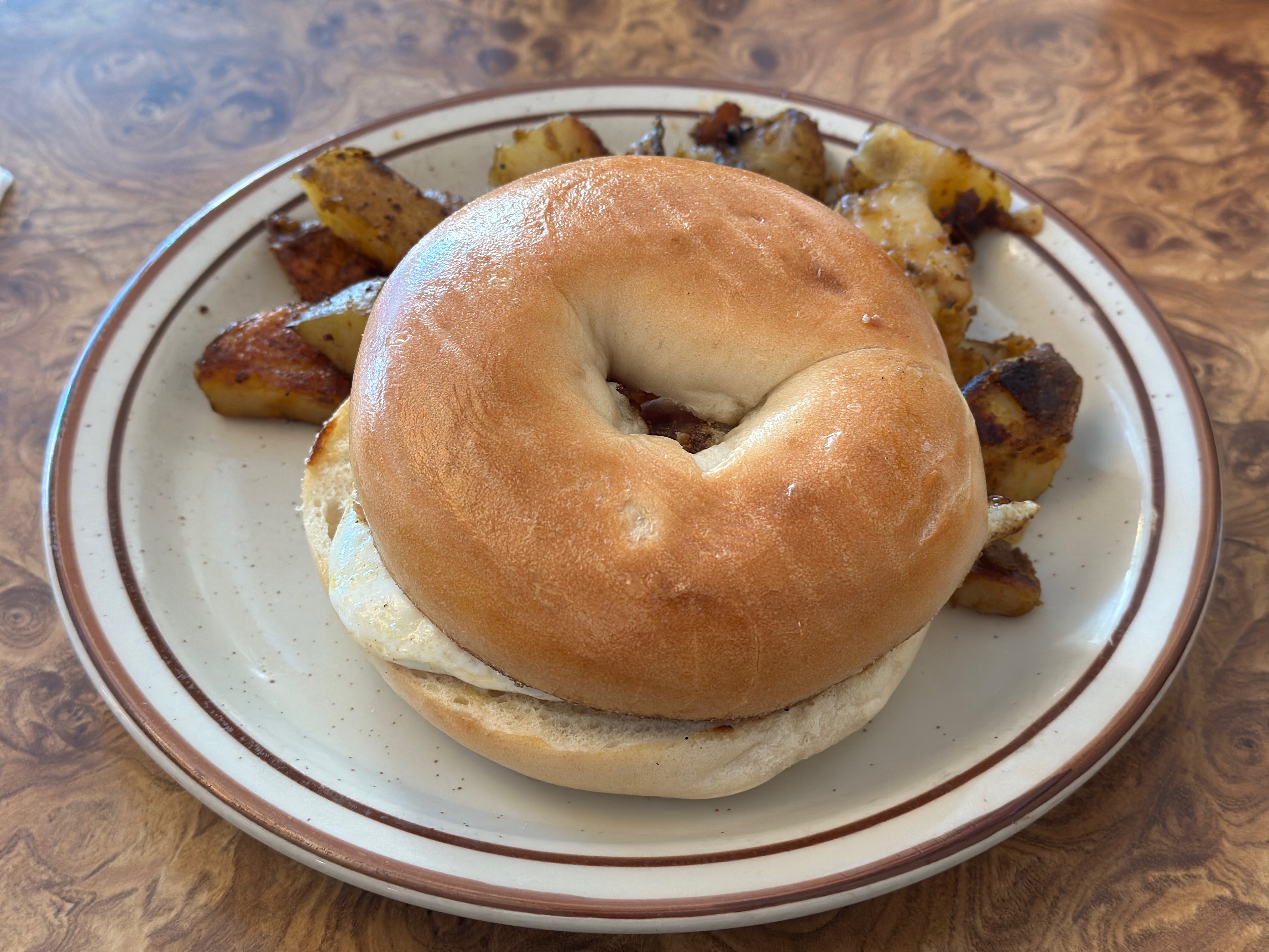 Bagel sandwich and potatoes on plate. 
