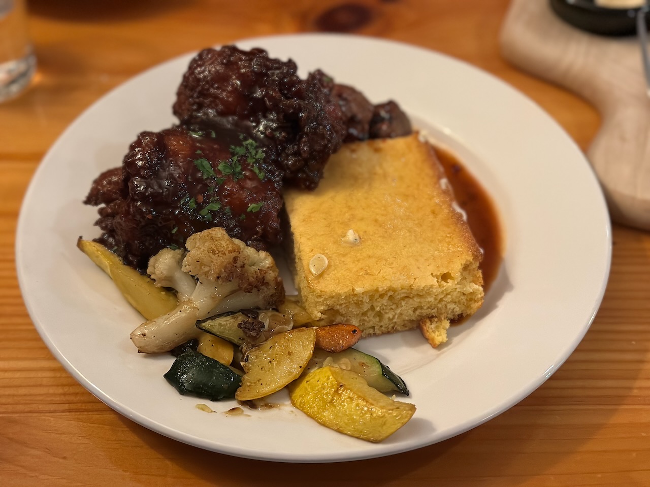 Short ribs, cornbread, and vegetables on plate. 