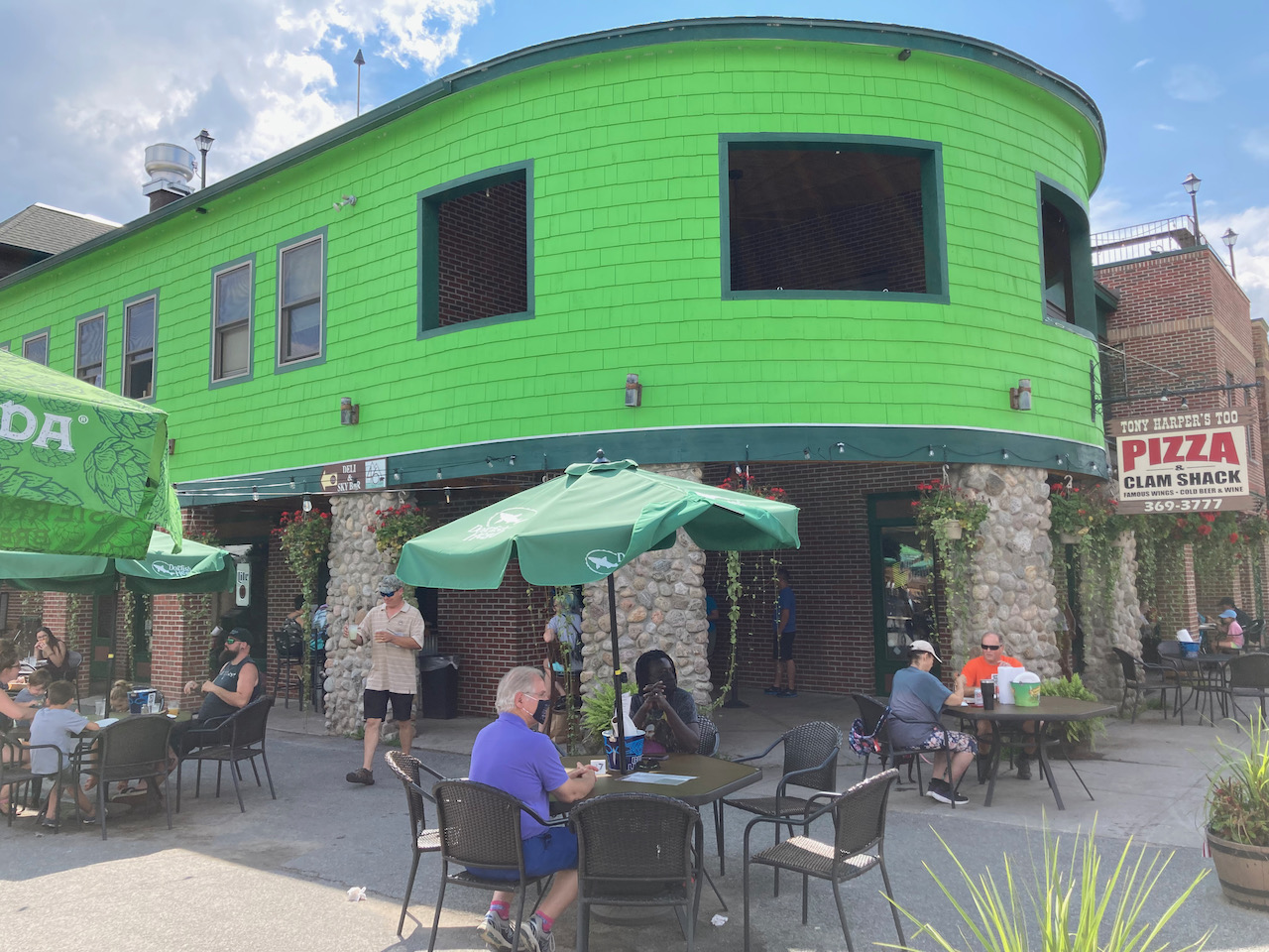 Exterior of Tony Harper's Pizzeria in Old Forge, with people sitting at tables beneath umbrellas in foreground. 