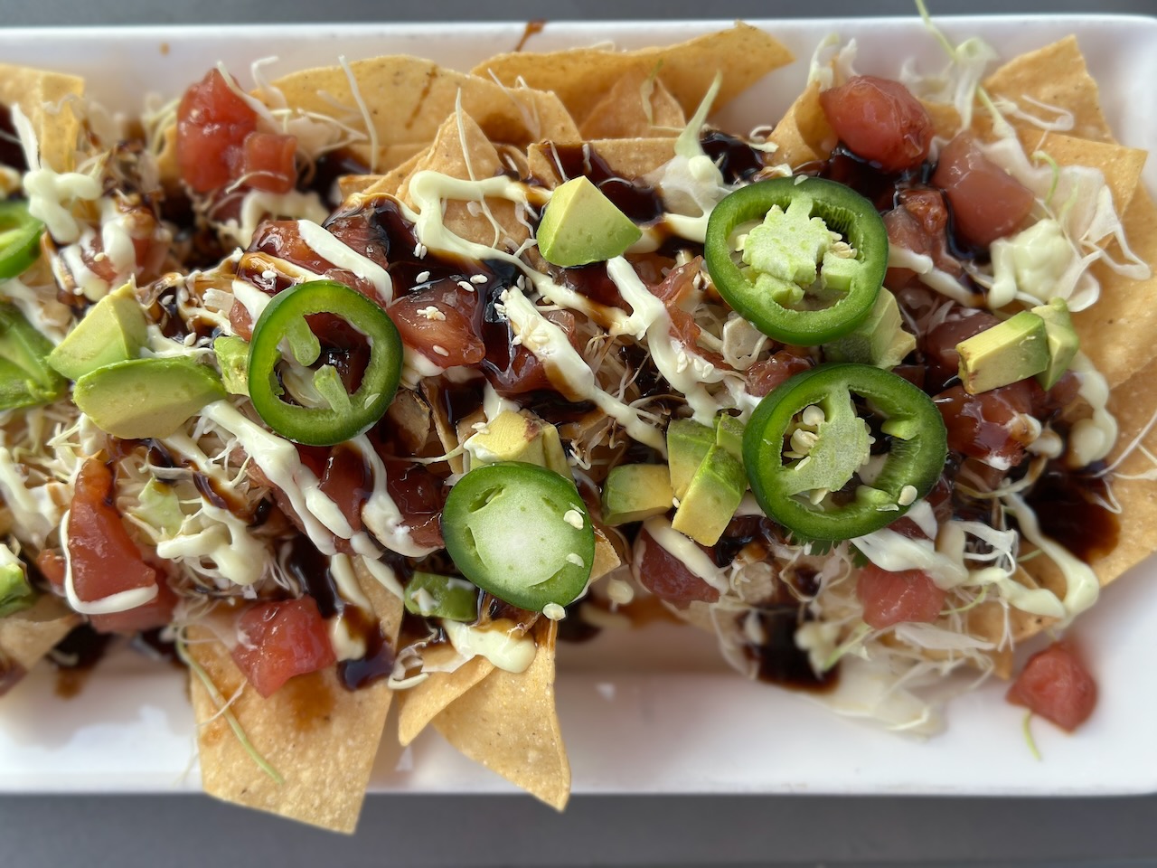 Tuna nachos covered in sauce, jalapeños, and other vegetables, on white plate. 