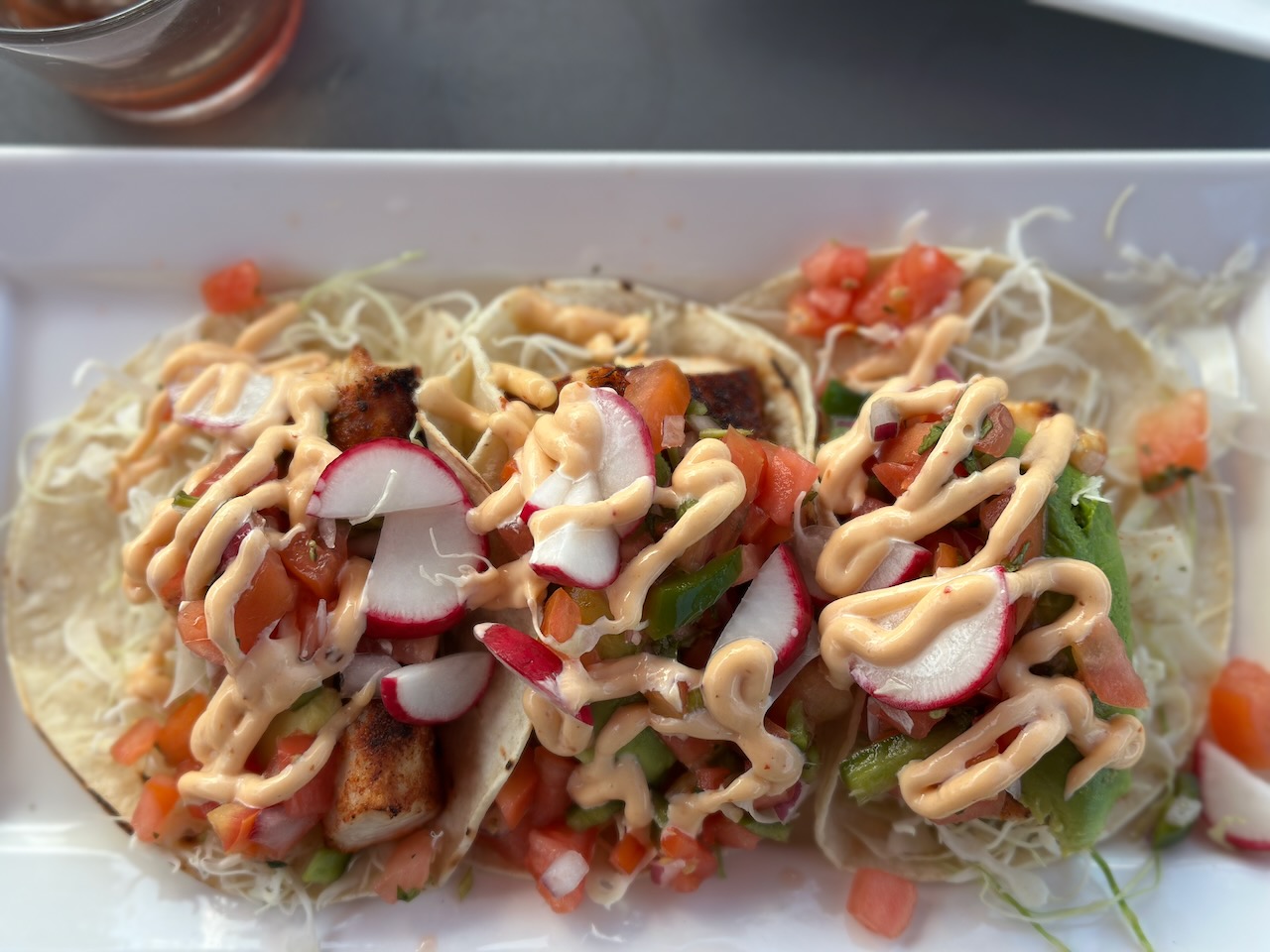 Three mahi mahi tacos on white plate. 