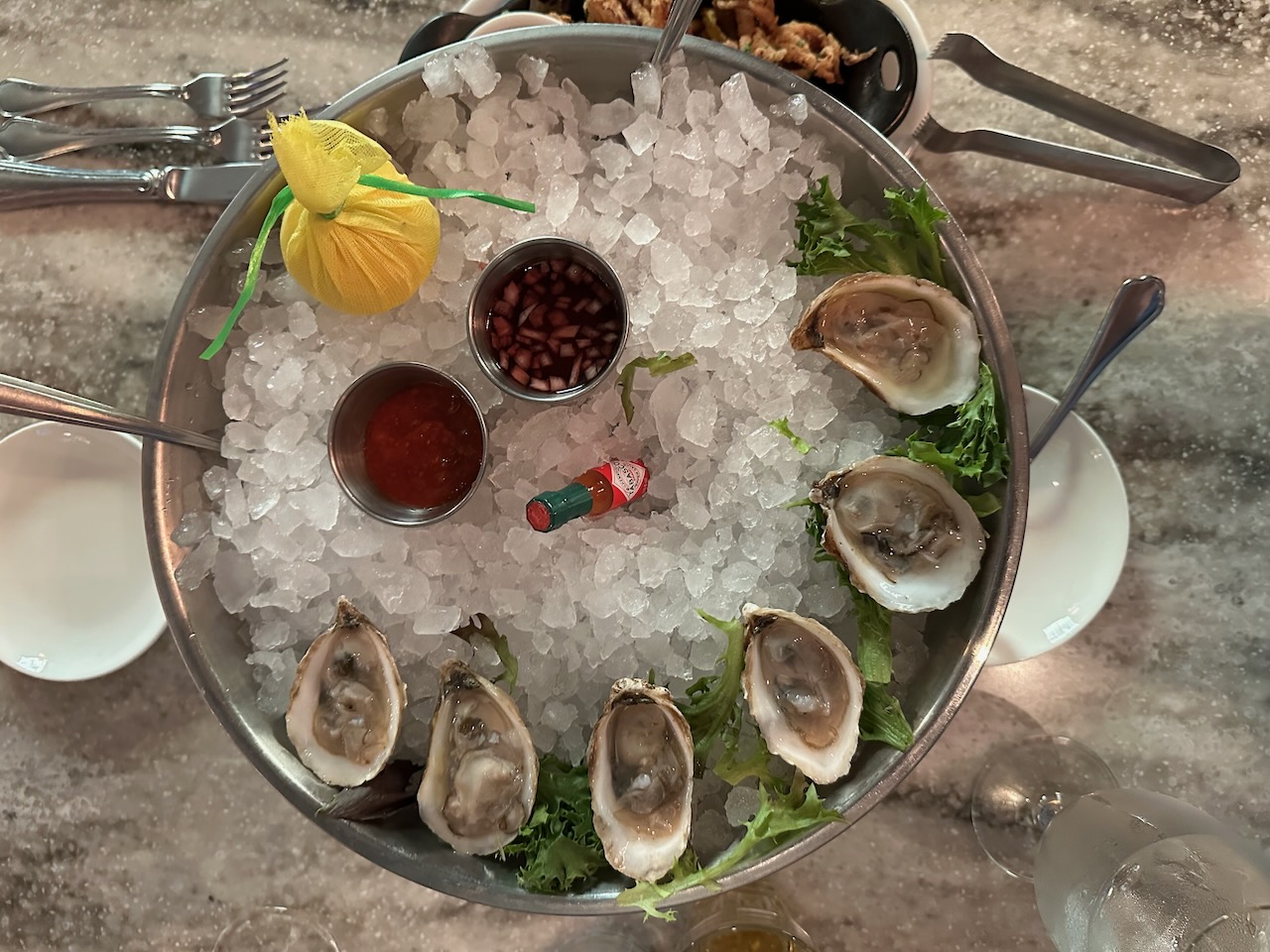 Half dozen oysters on ice in steel platter.