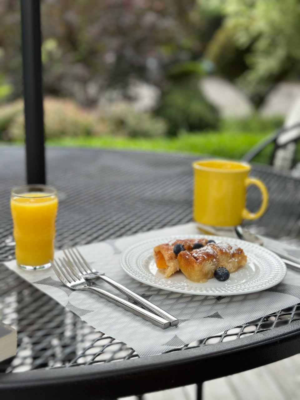 Glass of orange juice and mug of coffee on patio table, with pastry on white plate. 
