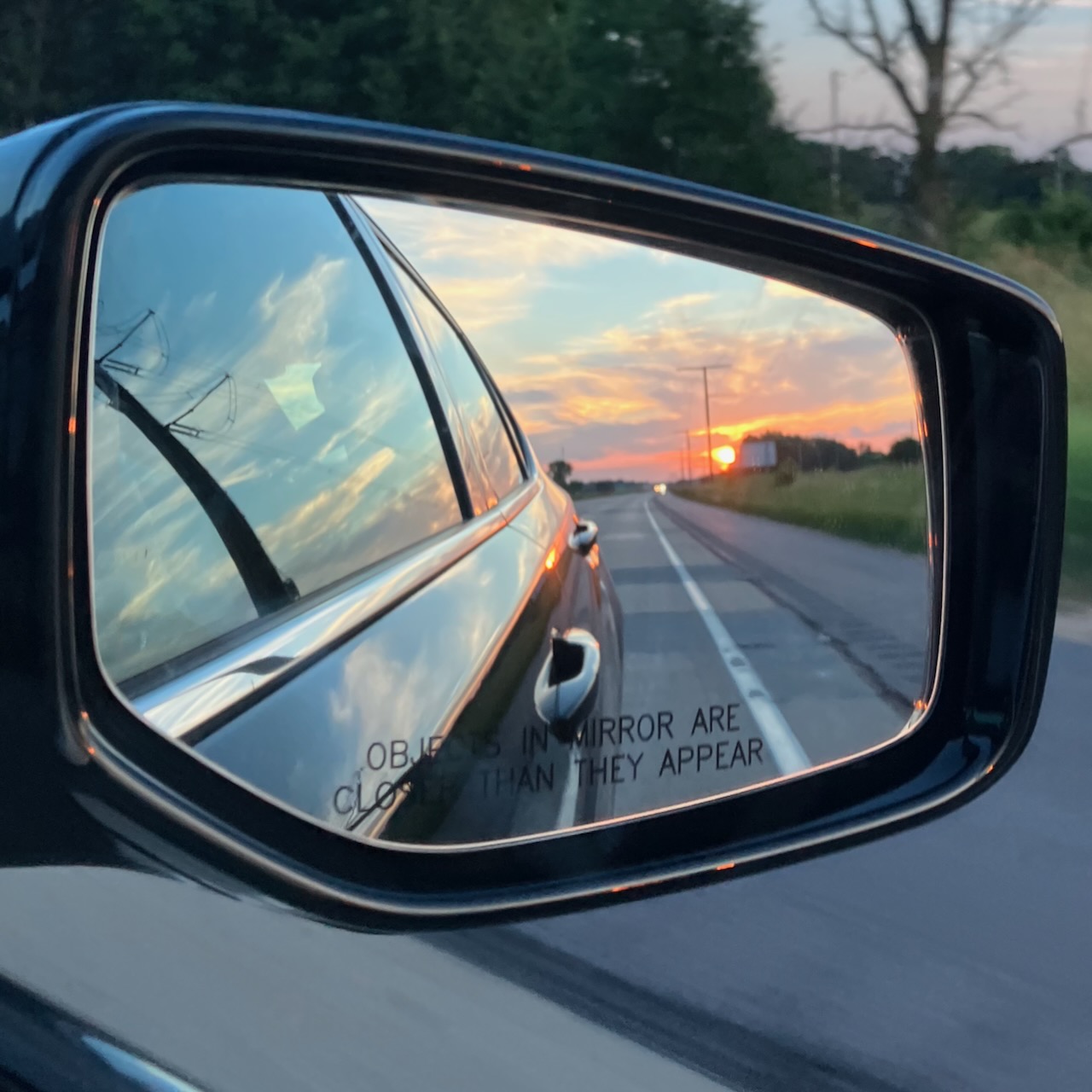Rear view mirror of 2020 Acura TLX with sun setting over road in reflection.