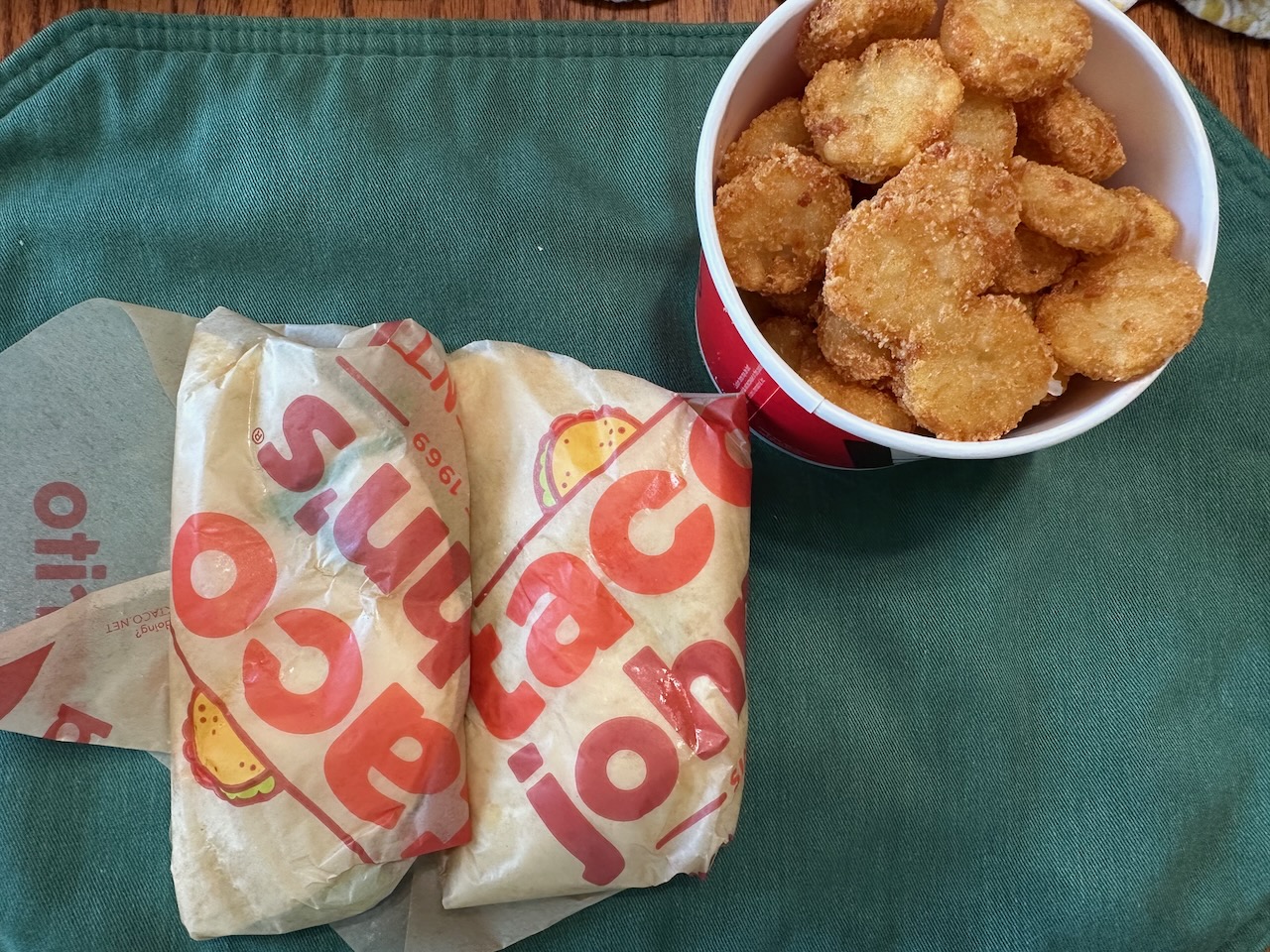 Two tacos in Taco Johns wrapping paper with bowl of potato oles.