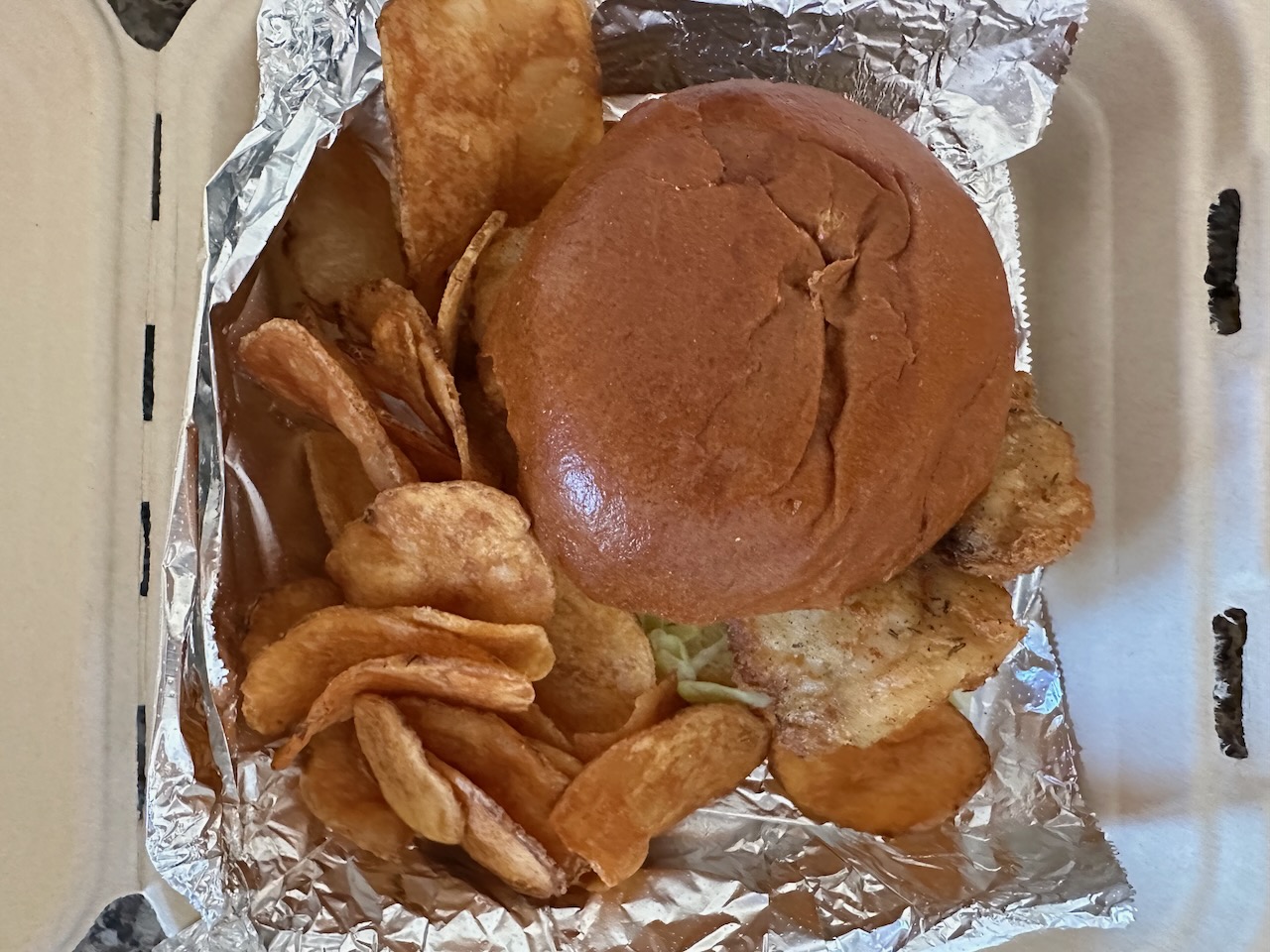 Beer-battered walleye sandwich and chips in to-go container.