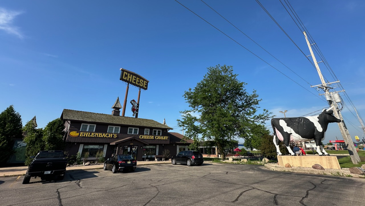 Exterior of Cheese Chalet with cow statue on right side of parking lot.