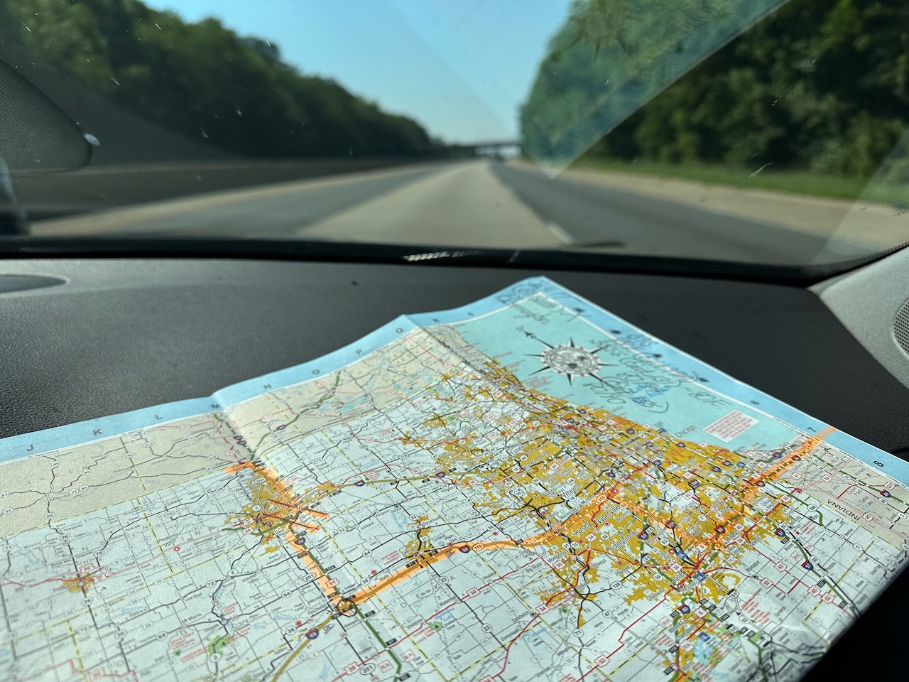 Paper map of Illinois on dashboard of car, with highway in view through windshield.