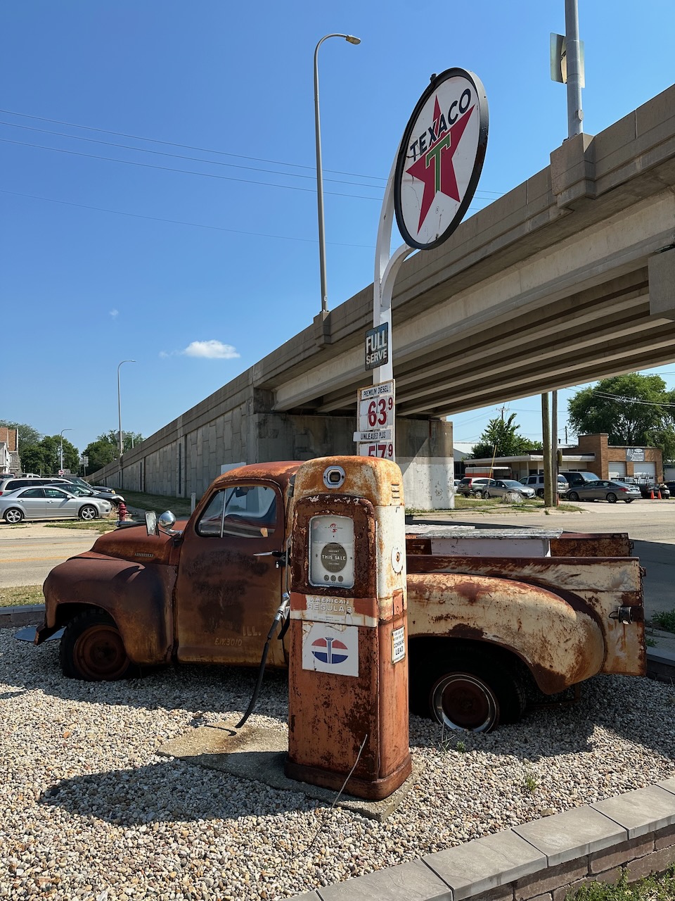 Rusty pickup truck and old gas pump on side of road.