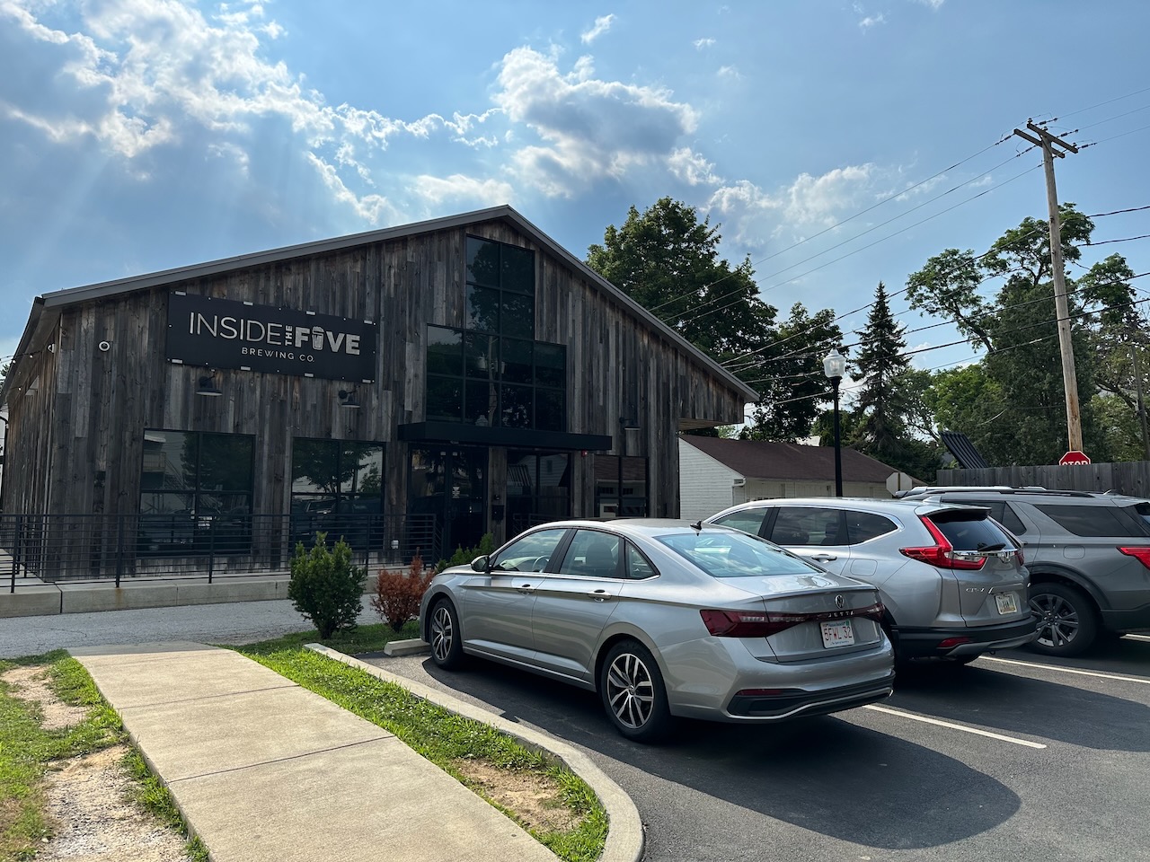 Exterior of Inside the Five Brewery, with cars parked in parking lot in front of building.
