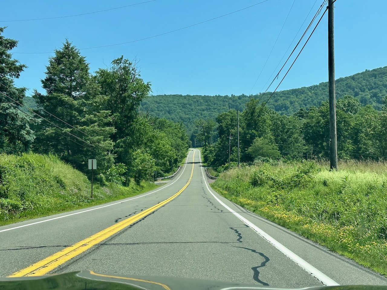 Two lane road in countryside, with hills in background.