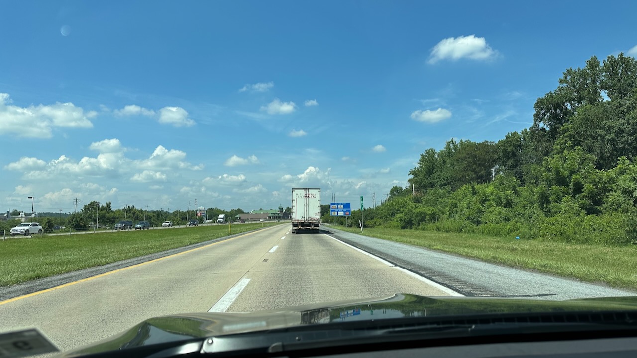 View of two-lane highway under blue skies. A tractor trailer is in distance.