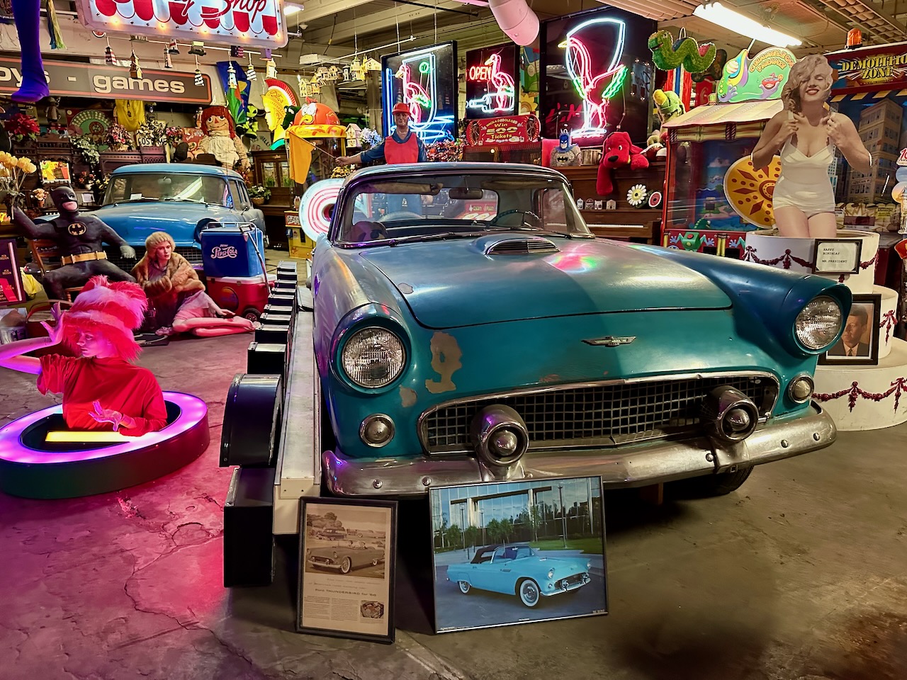 Blue Ford Thunderbird in foreground, with various pop culture artifacts on walls and hanging from ceiling in background.