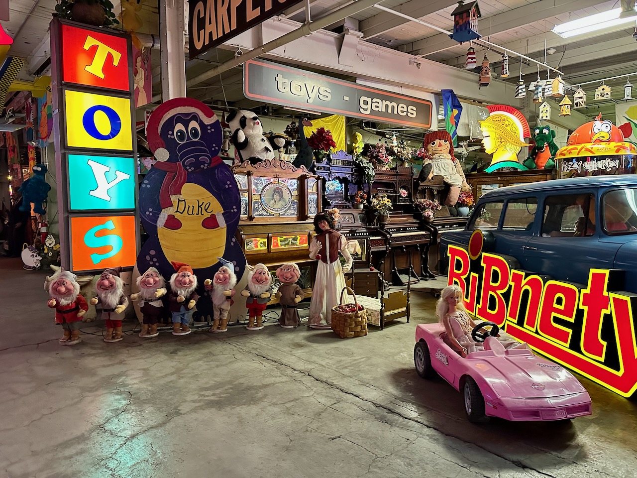 Museum space filled with toys, dolls, a car, and neon signs for stores and restaurants. 