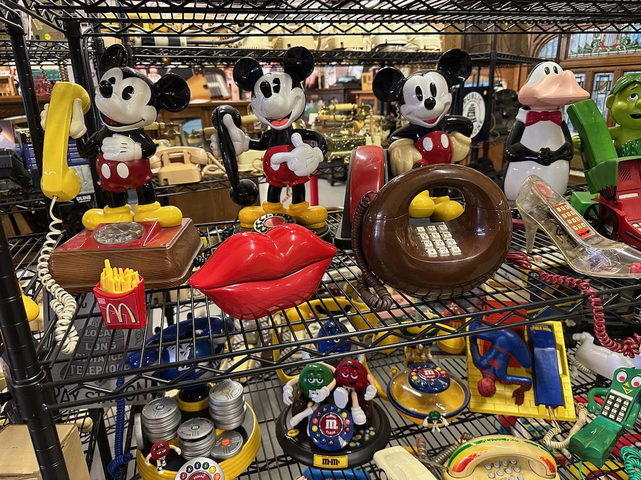 Toy and novelty telephones including Mickey Mouse phones on wire shelves.