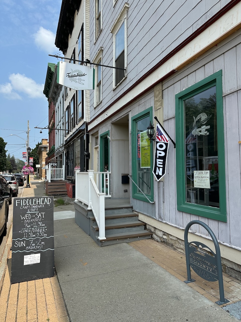 Exterior of restaurant with flag with OPEN sign by front door. 