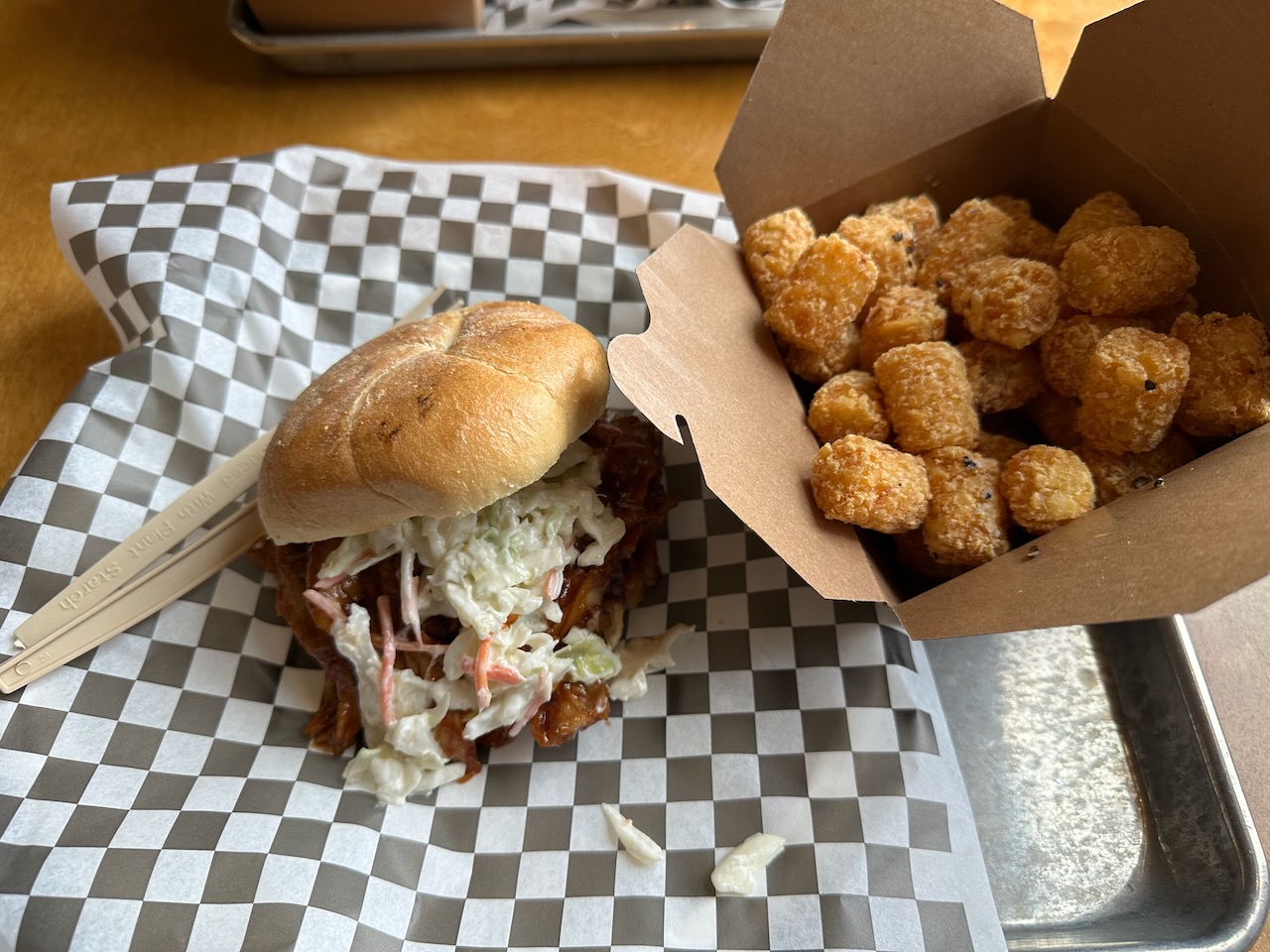 Pulled pork sandwich on bun, on paper plate, with a basket of tater tots beside it.