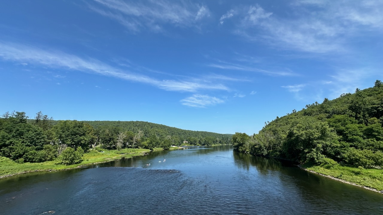 Delaware River with tree-lined banks, under a blue sky.