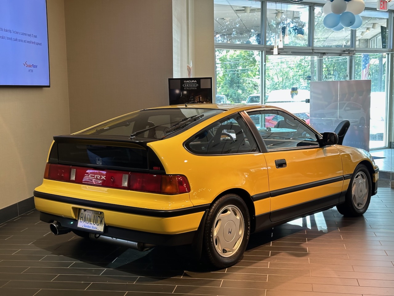2nd generation Honda CRX, in yellow, parked on dealership floor.