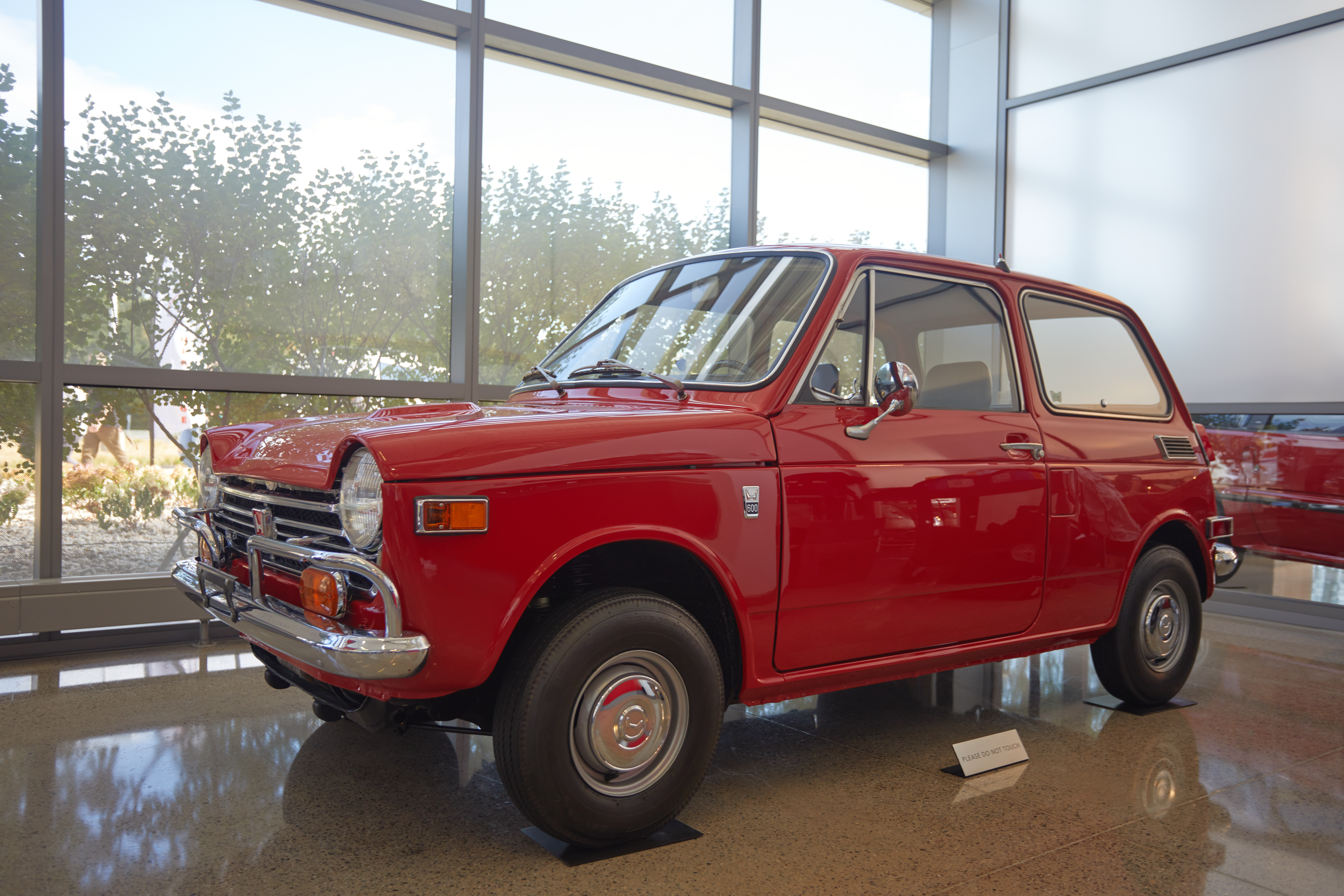 Honda N600, in red, parked by museum windows.