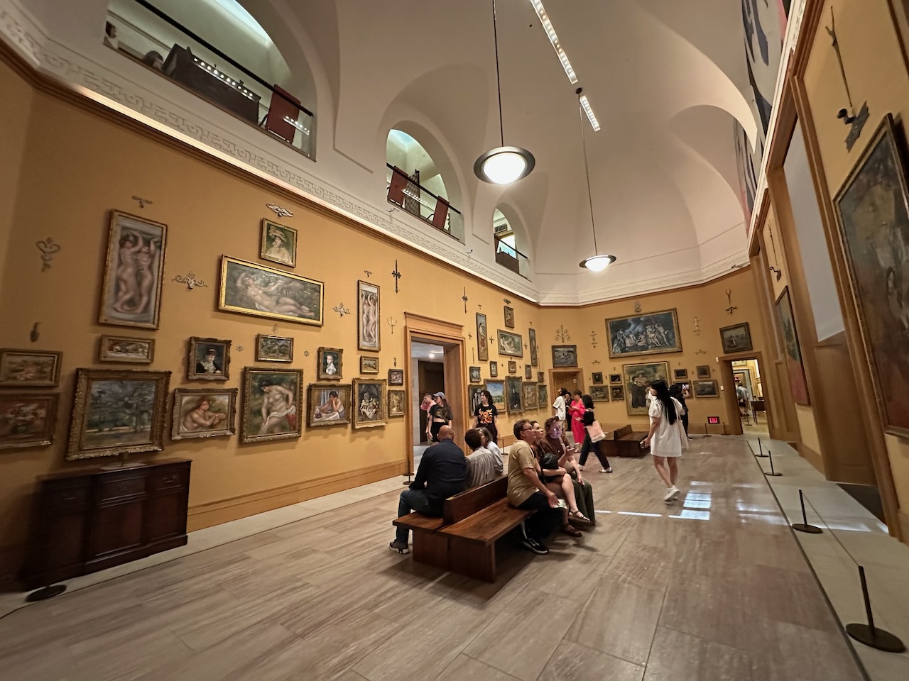 Interior of main collection hall within Barnes, with numerous paintings hung on walls. People are looking at the artwork.