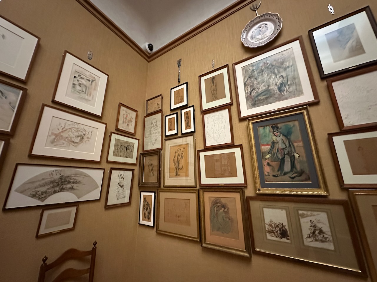 Numerous paintings and sketches on walls of museum in corner of room.