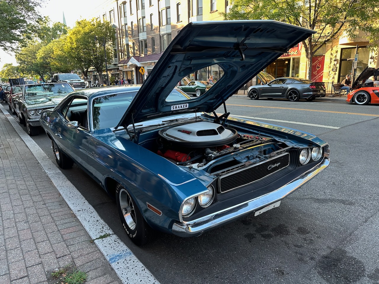Blue Dodge Challenger with hood up, parked along curb. 