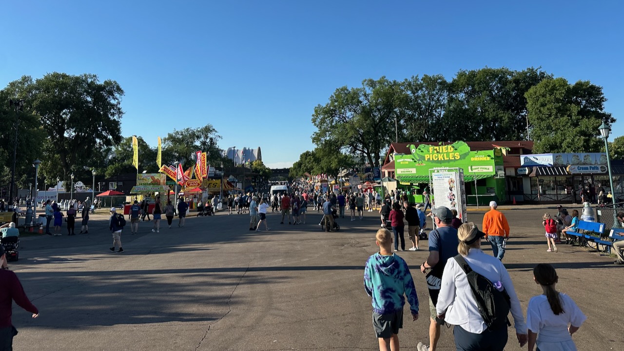 Fairgrounds, with small numbers of people walking down promenade.