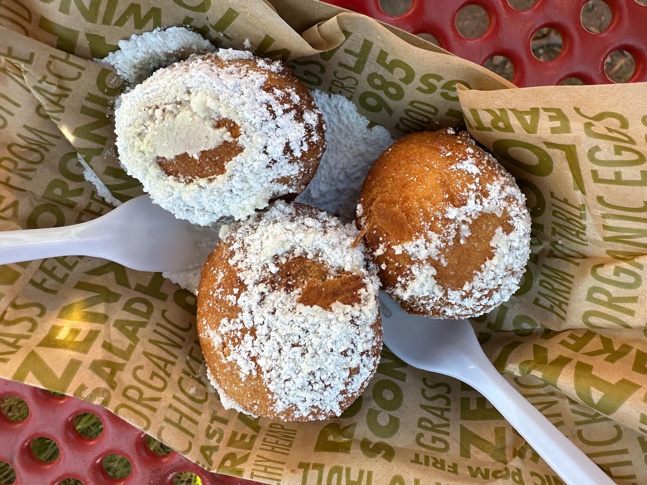 Small bite-size scones covered in powdered sugar, in basket with paper wrapper beneath.