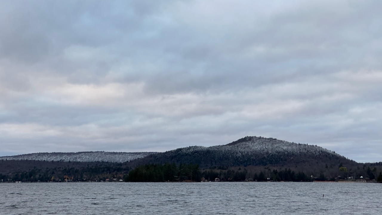 Lake in foreground, mountains in background. The mountaintops are covered in snow.