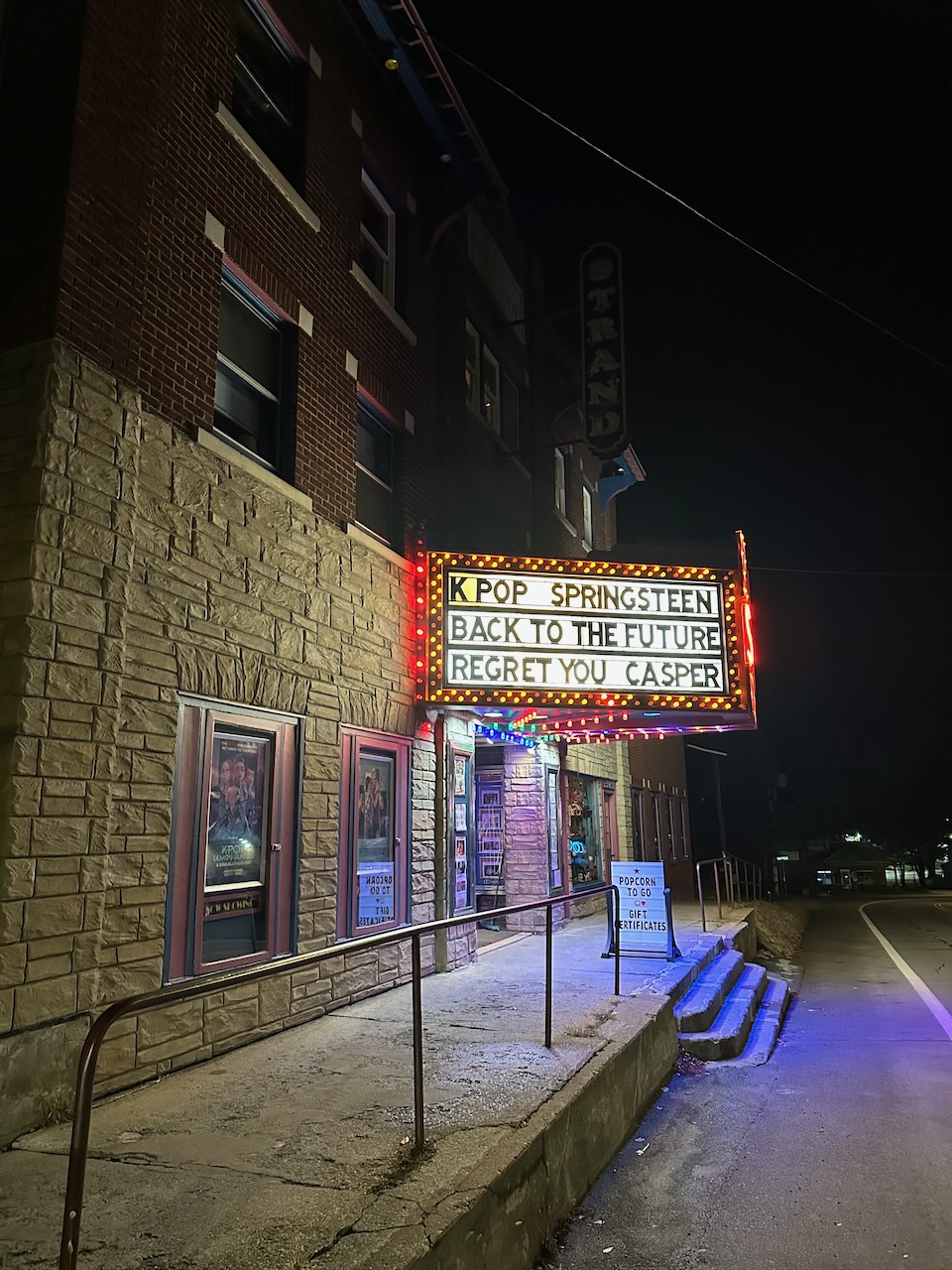 Exterior of The Strand movie theater, with marquee above door listing films currently showing.