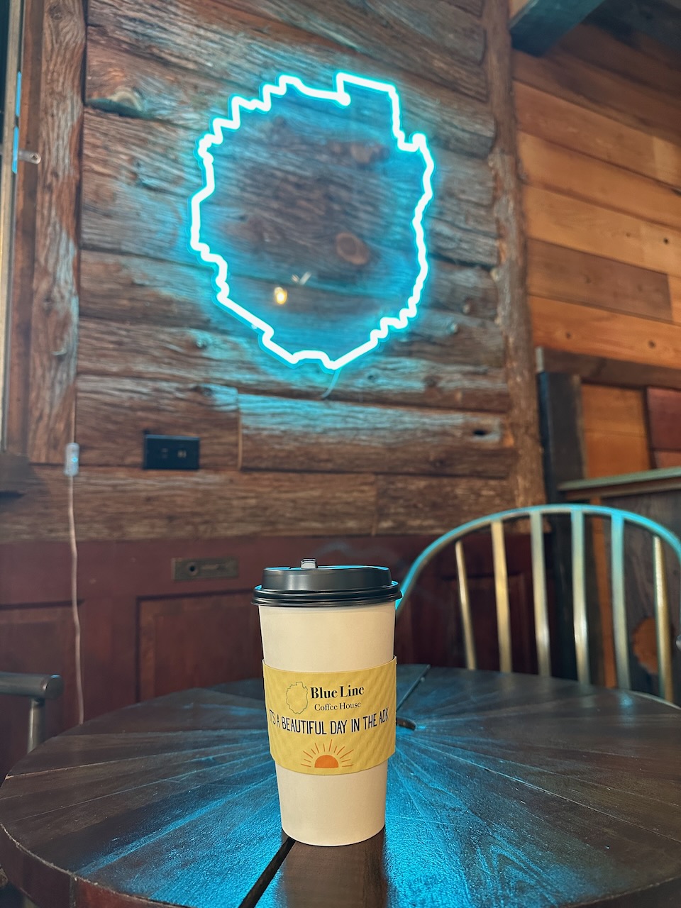 Coffee cup on table. On wall in background is a light-up sign of the outline of Adirondack State Park. 