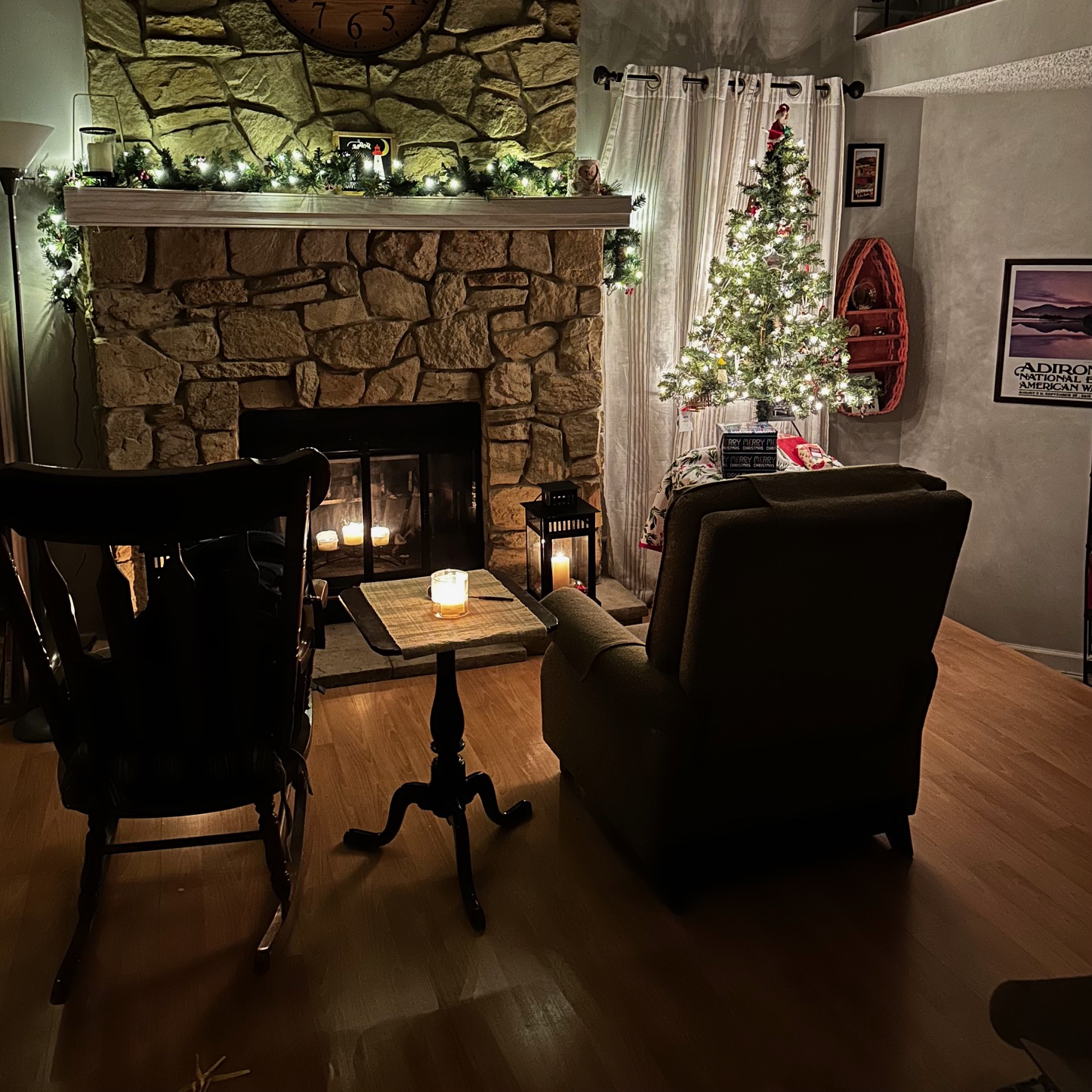 View of living room of house with Christmas tree beside fireplace. Two chairs are in foreground.